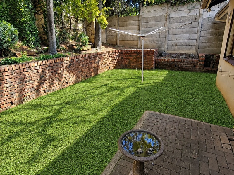 A private rear garden featuring a paved patio area, artificial lawn, brick retaining walls, and secure perimeter fencing.