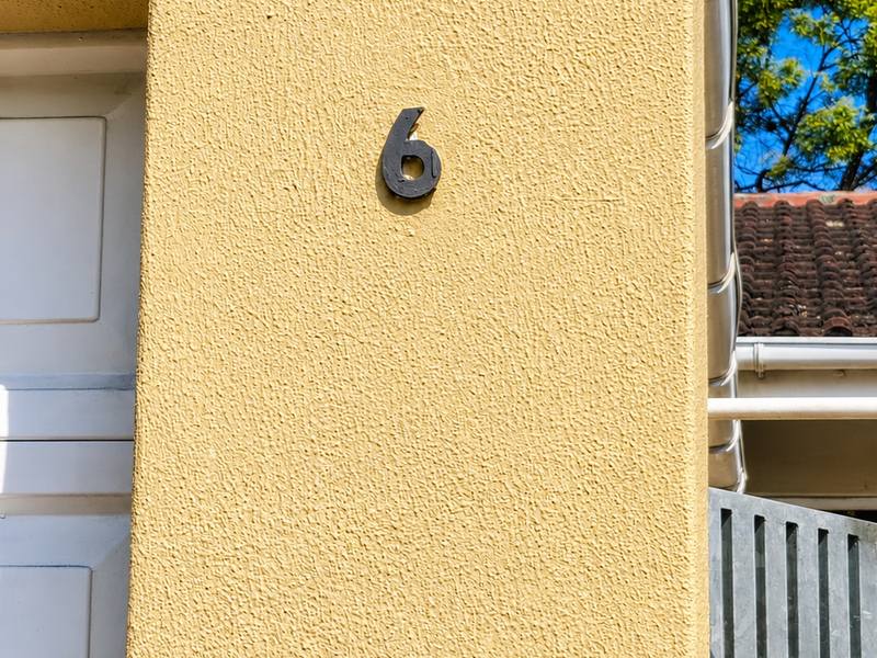 Close-up view of the townhouse exterior facade featuring textured yellow stucco, a garage door, and house number signage.