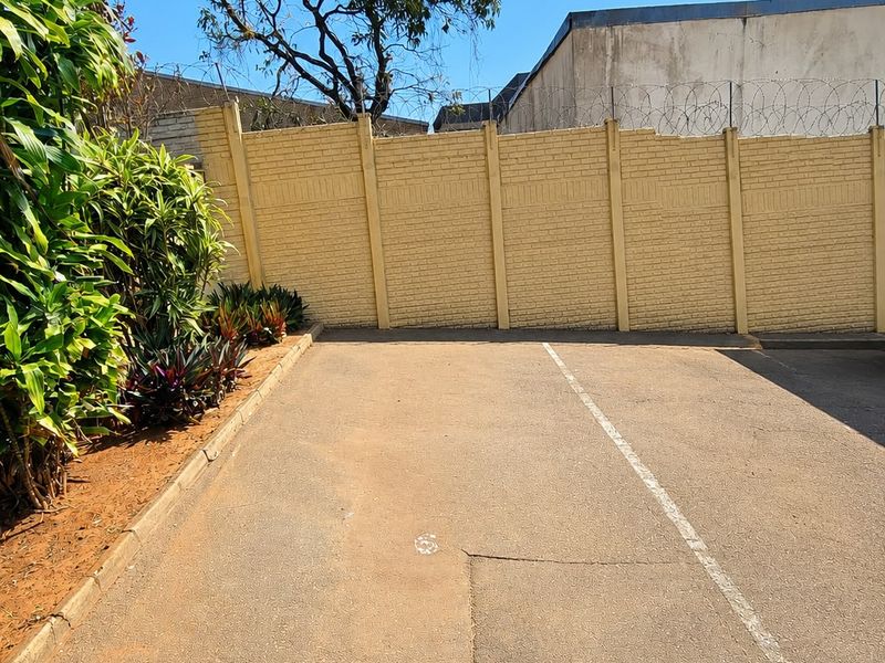 A paved outdoor parking or driveway area enclosed by a precast concrete boundary wall topped with security razor wire.