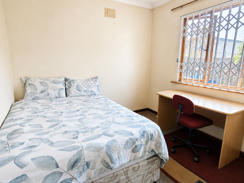 A functional bedroom featuring a ceiling fan and a window fitted with a security gate.