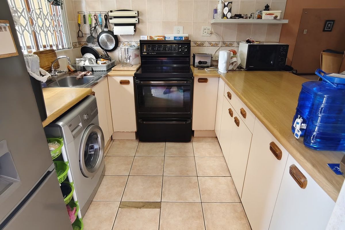 A functional kitchen featuring laminate countertops, built-in cabinetry, a tiled backsplash, and an electric stove, with tiled flooring throughout.