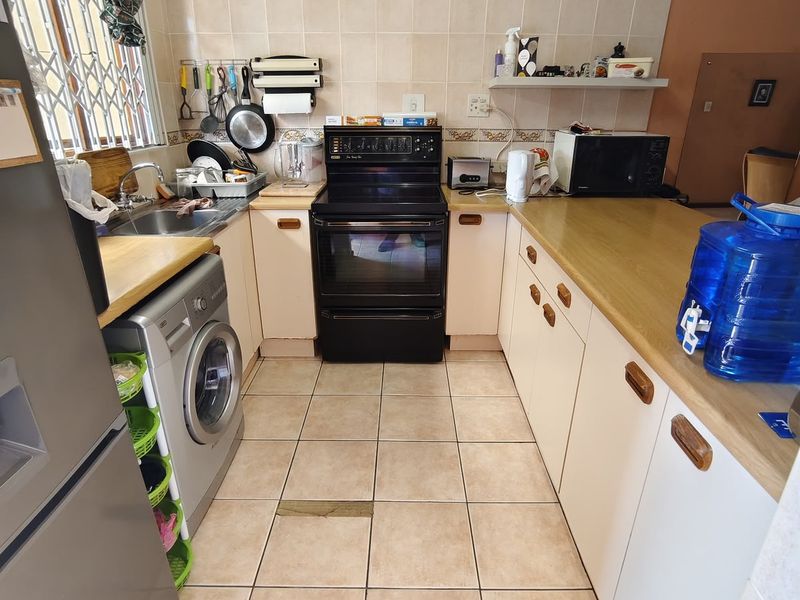 A functional kitchen featuring laminate countertops, built-in cabinetry, a tiled backsplash, and an electric stove, with tiled flooring throughout.