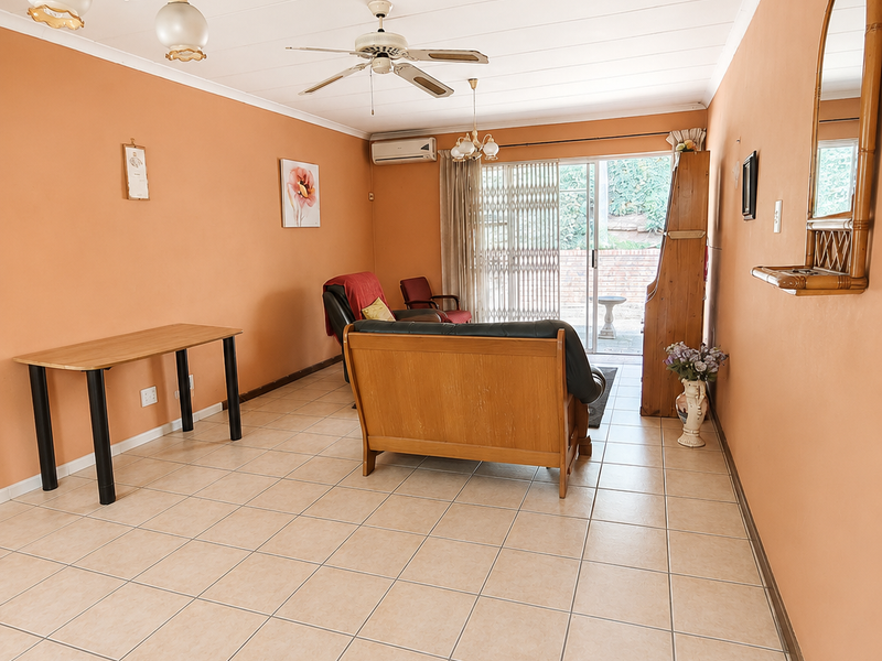 Spacious living room featuring neutral tiled flooring, a ceiling fan, split-system air conditioning, and sliding glass doors providing access to the outdoor area.