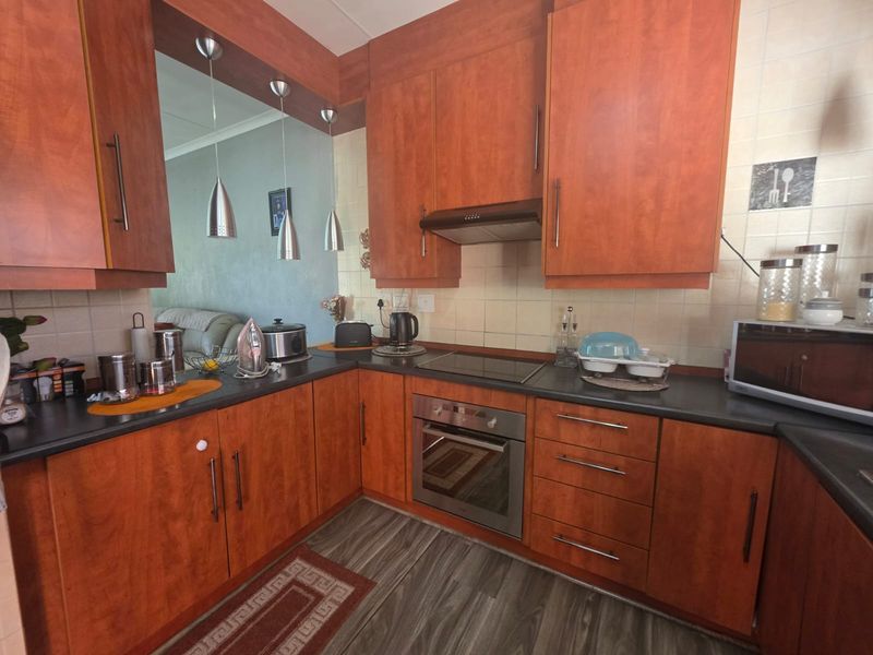 A functional kitchen featuring wood-look laminate cabinetry, dark countertops, a built-in oven with electric cooktop, and a tiled backsplash.