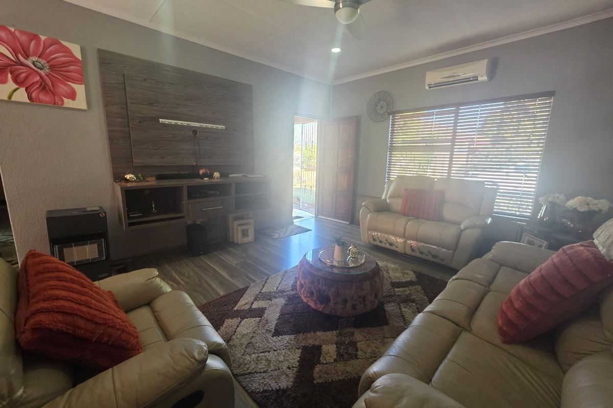 A comfortable living room featuring laminate flooring, a built-in media console, ceiling fan, and a wall-mounted air conditioning unit.