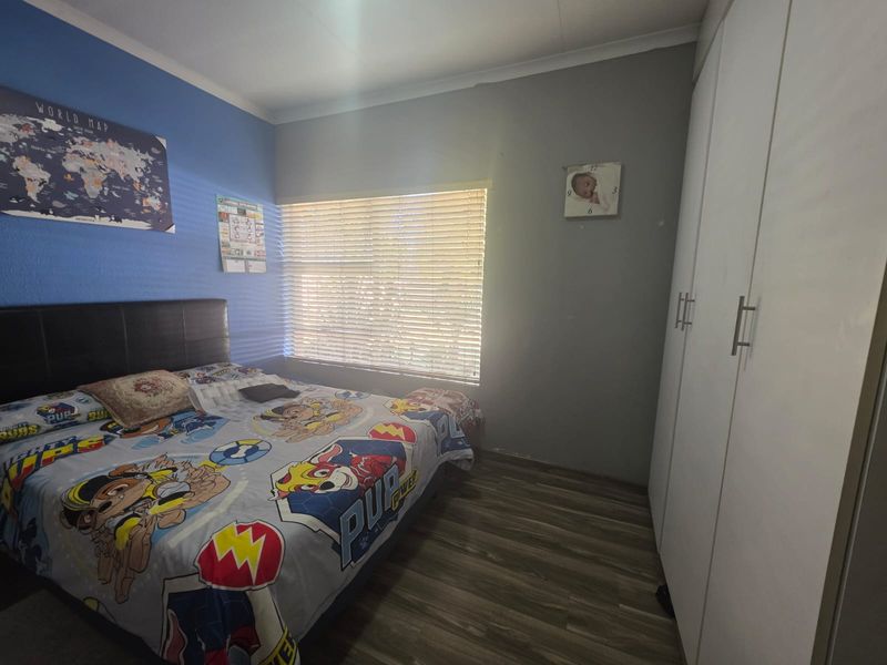 A functional bedroom featuring laminate flooring, built-in cupboards, and venetian blinds, providing a practical space with neutral wall finishes.