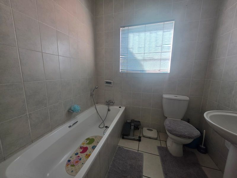 A functional bathroom featuring a bathtub with handheld shower mixer, pedestal basin, and toilet, finished with neutral wall and floor tiling.