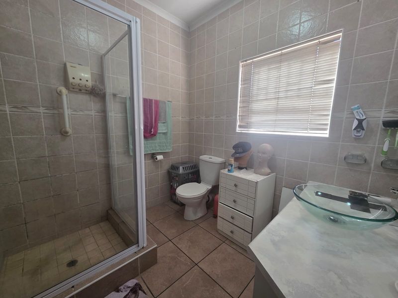 A dated bathroom featuring a shower enclosure, toilet, and glass vessel basin with tiled walls and flooring throughout.