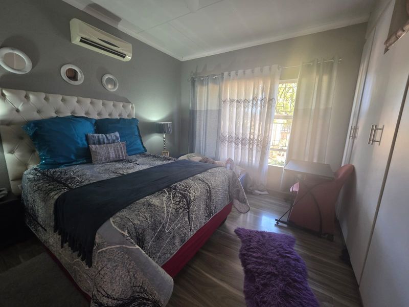 A well-lit bedroom featuring laminate flooring, built-in cupboards, and a wall-mounted split-system air conditioning unit.