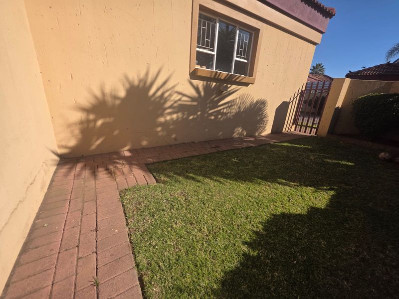 A rear garden area featuring a paved walkway, a small lawn, and a secure gated access point along the exterior wall.