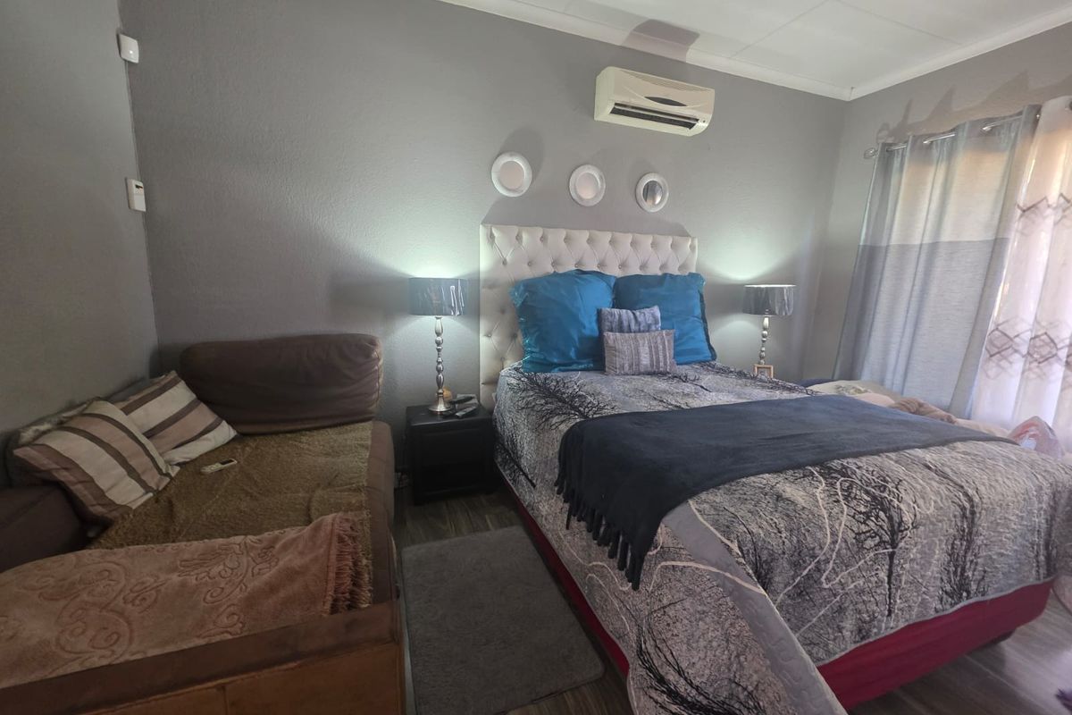 A functional bedroom featuring laminate flooring, an installed air conditioning unit, and neutral wall finishes, providing a comfortable space for rest.