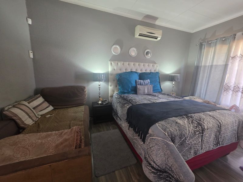 A functional bedroom featuring laminate flooring, an installed air conditioning unit, and neutral wall finishes, providing a comfortable space for rest.