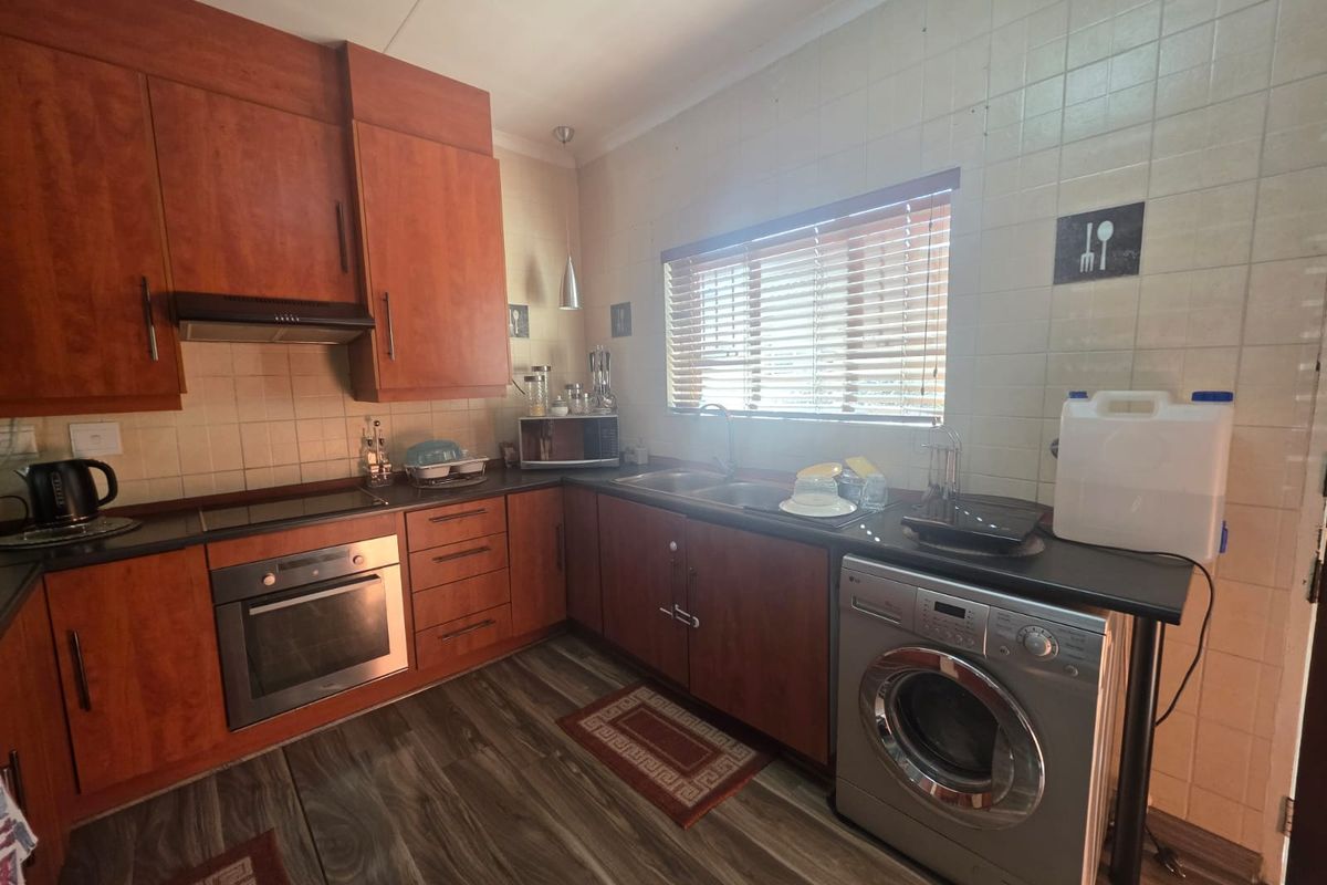 A functional kitchen featuring wood-tone cabinetry, dark laminate countertops, a built-in oven, extractor fan, and dedicated space for laundry appliances.