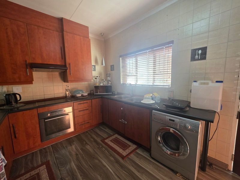 A functional kitchen featuring wood-tone cabinetry, dark laminate countertops, a built-in oven, extractor fan, and dedicated space for laundry appliances.