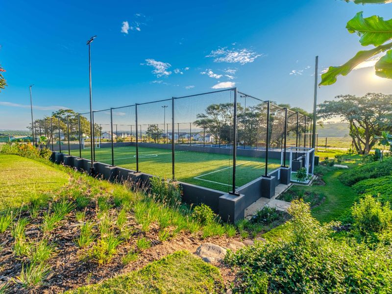 A well-maintained outdoor sports facility featuring artificial turf, perimeter fencing, and integrated floodlights, set within a landscaped residential environment.