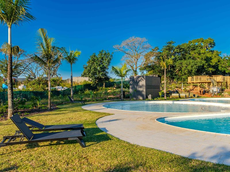 A well-maintained outdoor pool area featuring a paved deck, lush green lawn, and a wooden play structure set within a landscaped garden.