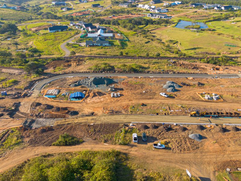 Aerial view of a residential development site showing ongoing road construction, utility installation, and cleared plots ready for building.
