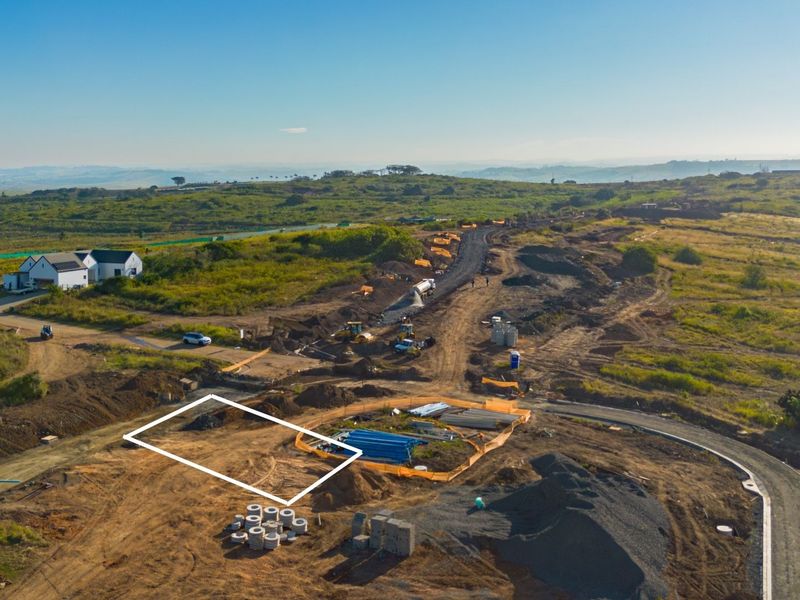 Aerial view of a residential development site showing cleared land, ongoing road construction, and surrounding landscape.