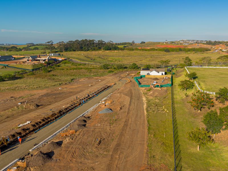 Aerial view of a residential development site showing ongoing road construction, utility installation, and surrounding vacant land.