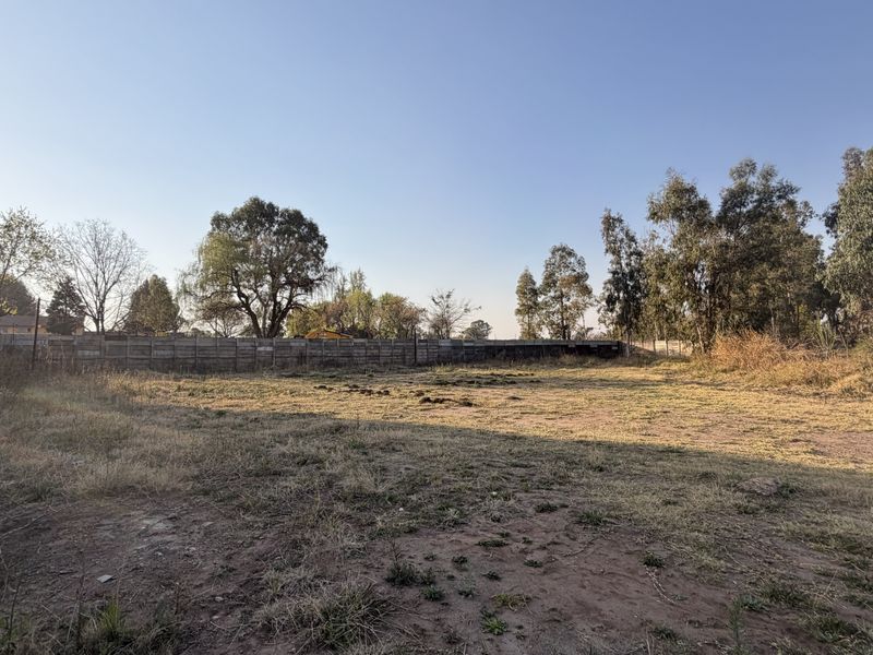 A large, undeveloped plot of land enclosed by precast concrete walling and electric fencing, featuring natural grass and mature trees.