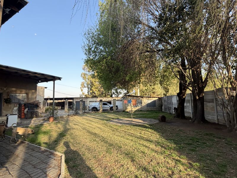 A spacious rear garden area featuring a covered patio, paved walkways, and perimeter precast walling, with access to outbuildings and storage structures.