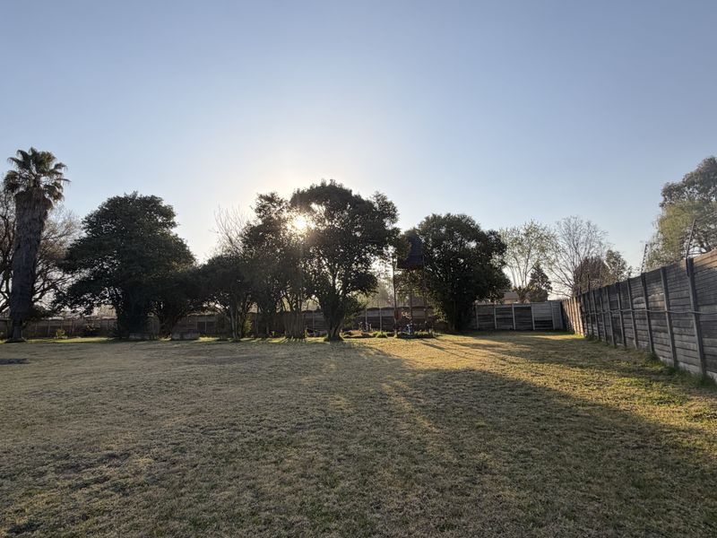 A spacious, level garden area featuring mature trees and secure perimeter walling with electric fencing.