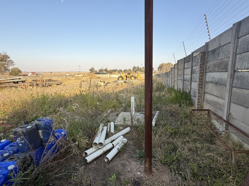 An expansive outdoor area featuring a precast concrete boundary wall with electric fencing, showing signs of neglect and overgrown vegetation.