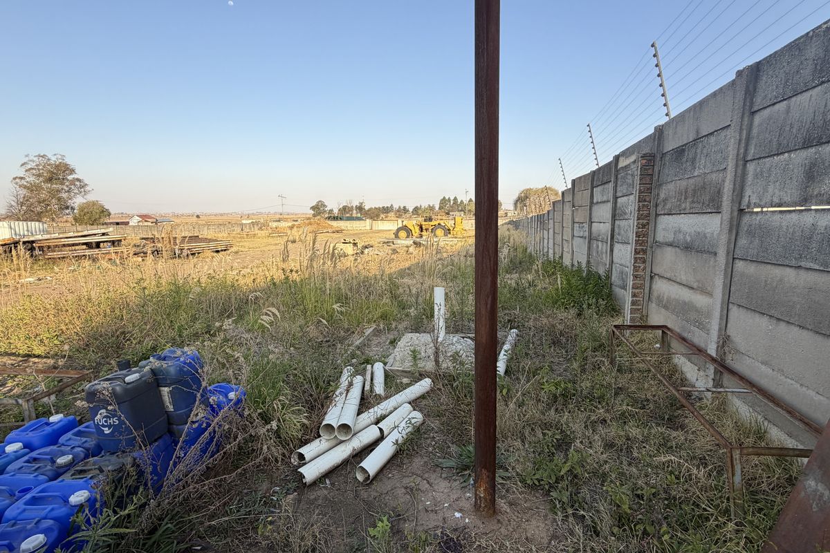An expansive outdoor area featuring a precast concrete boundary wall with electric fencing, showing signs of neglect and overgrown vegetation.