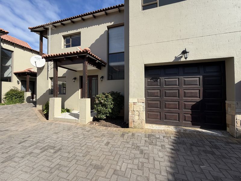 Front elevation of a townhouse featuring a paved driveway, integrated garage, and a covered entrance porch with tiled roof detailing.