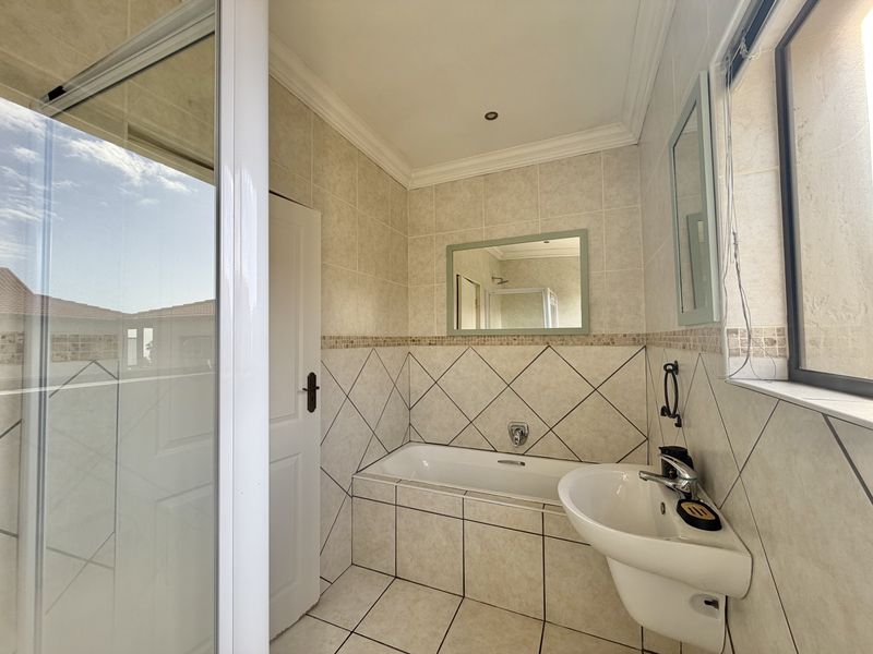 A clean, well-maintained bathroom featuring a built-in bathtub, wall-mounted basin, and a separate shower enclosure with neutral floor-to-ceiling tiling.