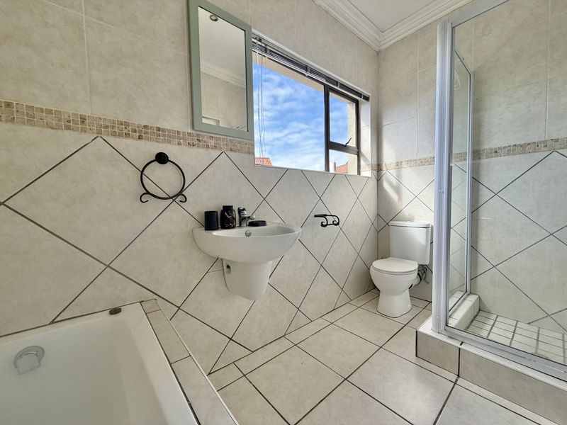A functional bathroom featuring a shower enclosure, bathtub, wall-mounted basin, and toilet with neutral tiled finishes and natural light.