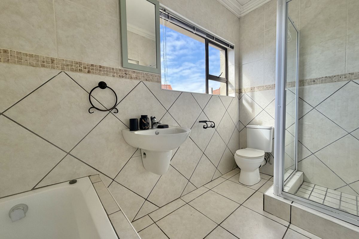 A functional bathroom featuring a shower enclosure, bathtub, wall-mounted basin, and toilet with neutral tiled finishes and natural light.