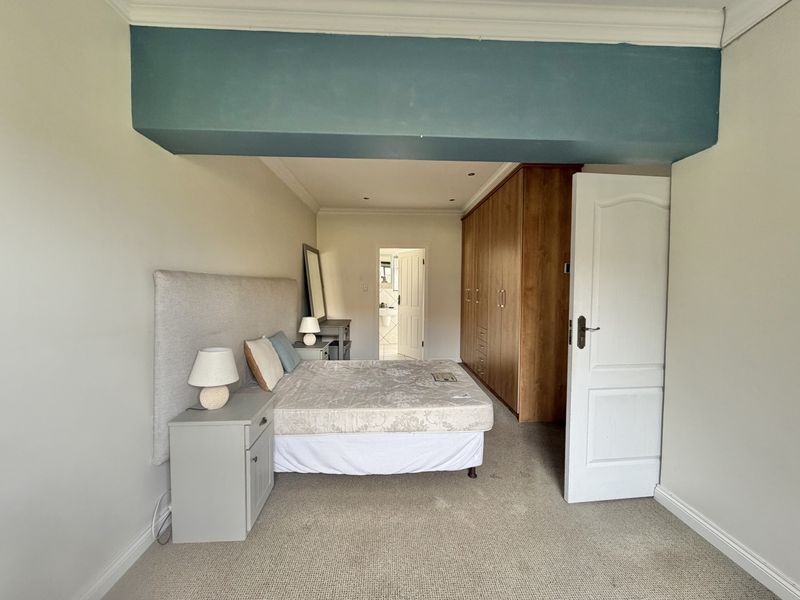Spacious bedroom featuring built-in wooden cupboards, neutral carpeting, and recessed lighting, with an adjoining doorway leading to an en-suite bathroom.