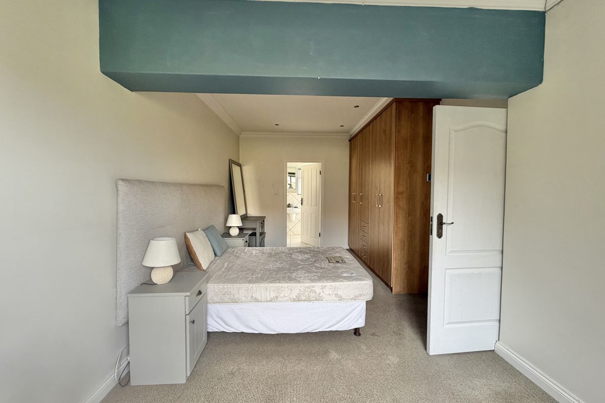Spacious bedroom featuring built-in wooden cupboards, neutral carpeting, and recessed lighting, with an adjoining doorway leading to an en-suite bathroom.