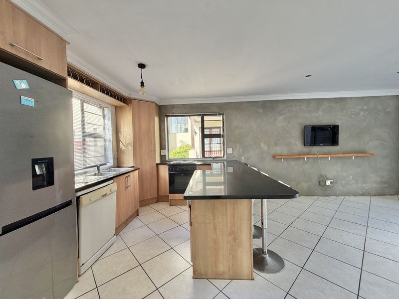 Open-plan kitchen featuring wood-finish cabinetry, granite countertops, a central island, and tiled flooring, with an adjacent living area featuring a textured feature wall.