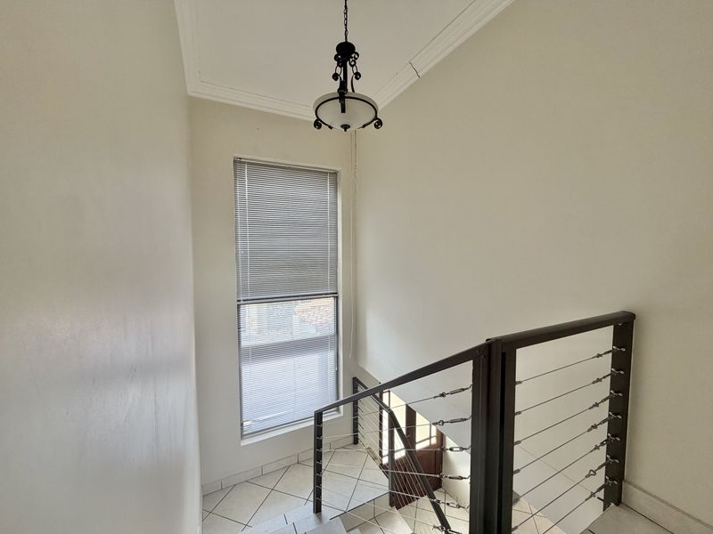 A bright stairwell featuring tiled flooring, a modern cable railing system, and a tall window with venetian blinds.