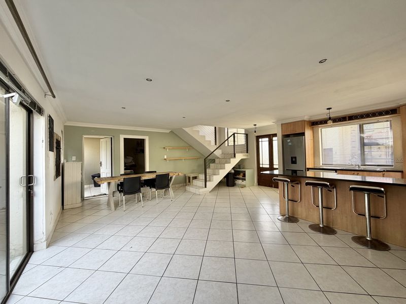 Spacious open-plan living and kitchen area featuring tiled flooring, a central staircase, and direct access to the outdoors through sliding glass doors.