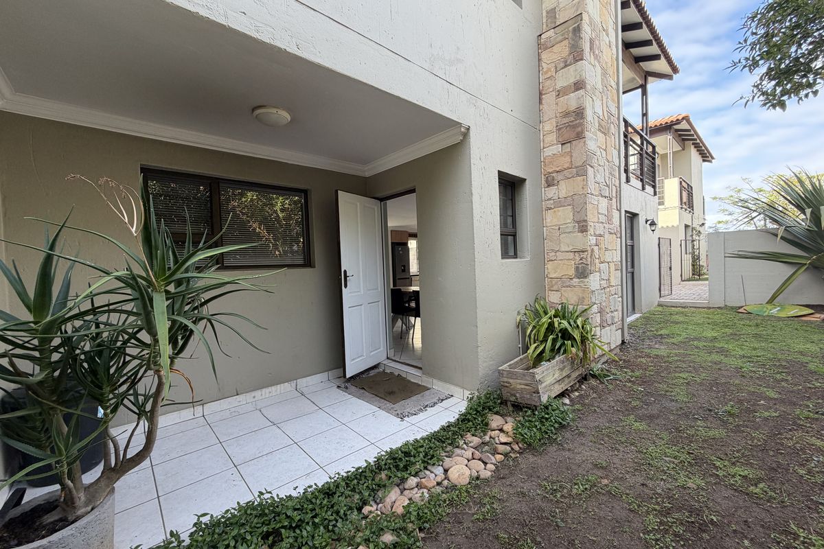 Rear view of the townhouse featuring a tiled patio, stone-clad chimney detail, and access to the garden area.
