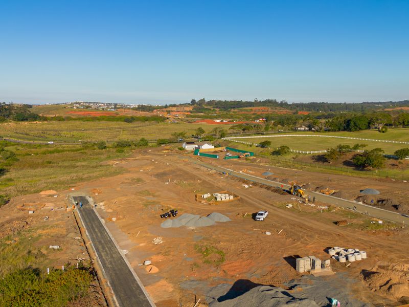 Aerial view of a residential development site showing ongoing road construction, earthworks, and surrounding landscape.