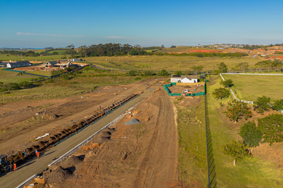 Aerial view of a residential development site showing ongoing road construction, utility installation, and surrounding vacant land.