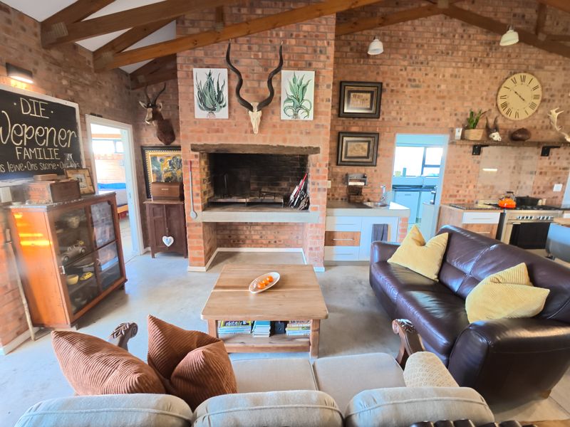 Spacious open-plan living area featuring exposed brick walls, timber beams, a large built-in indoor braai, and an integrated kitchen space.