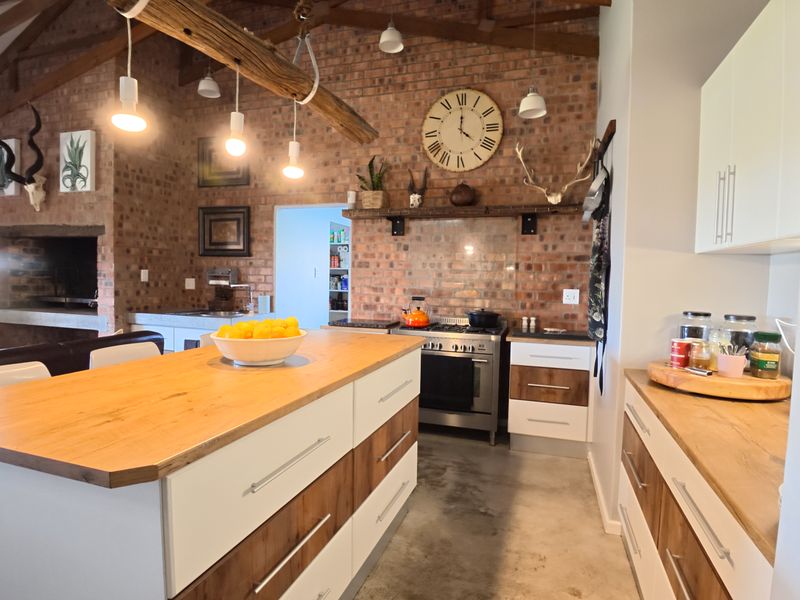 Spacious kitchen featuring exposed brick walls, timber beams, a central island with timber countertop, gas stove, and polished concrete flooring.