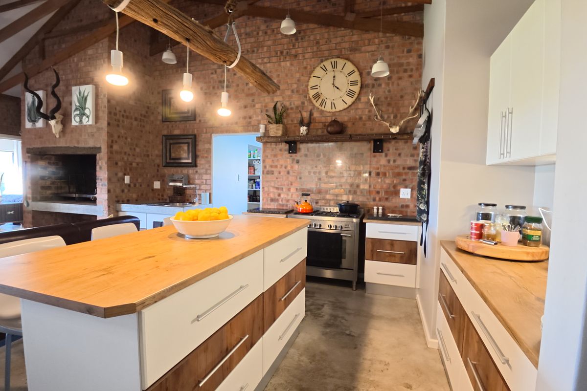 Spacious kitchen featuring exposed brick walls, timber beams, a central island with timber countertop, gas stove, and polished concrete flooring.