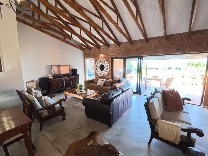 Spacious living room featuring exposed timber rafters, a rustic brick feature wall, and large bi-fold doors opening to an outdoor patio area.