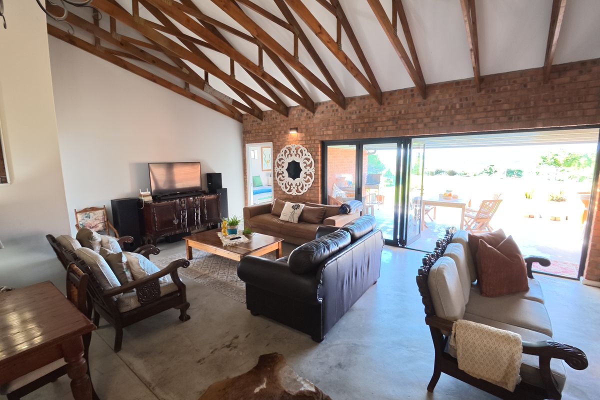 Spacious living room featuring exposed timber rafters, a rustic brick feature wall, and large bi-fold doors opening to an outdoor patio area.