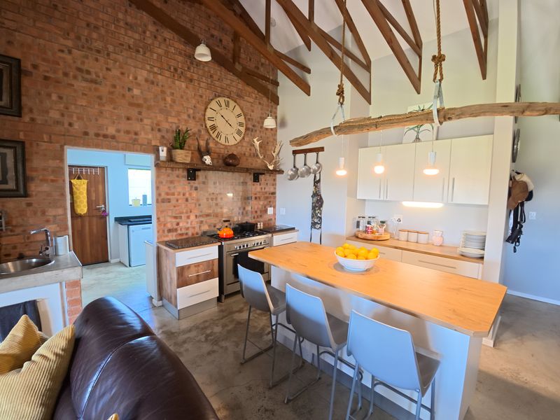 Spacious open-plan kitchen featuring exposed brick walls, timber rafters, a central island, and modern cabinetry, seamlessly connecting to a secondary utility area.