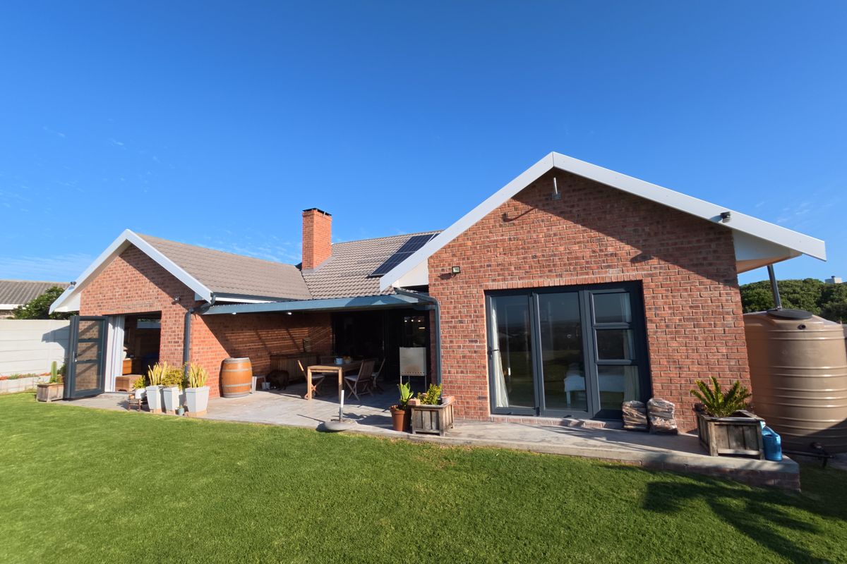 Rear view of a brick house featuring a covered patio area, bi-fold doors, and a well-maintained lawn.