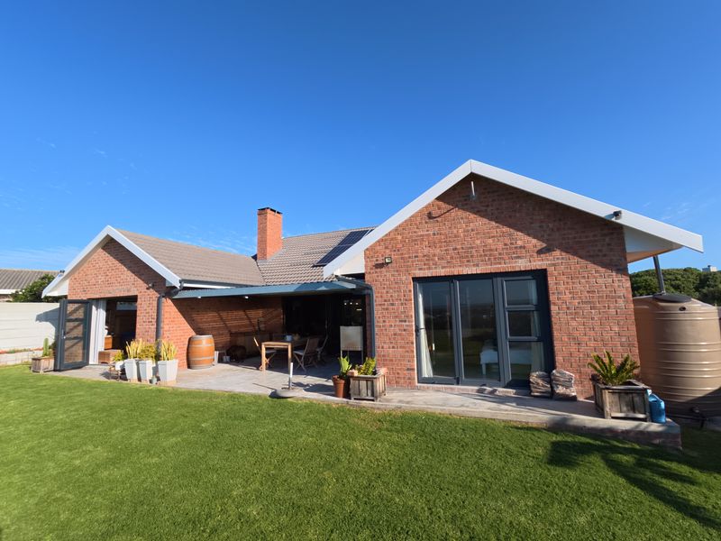 Rear view of a brick house featuring a covered patio area, bi-fold doors, and a well-maintained lawn.
