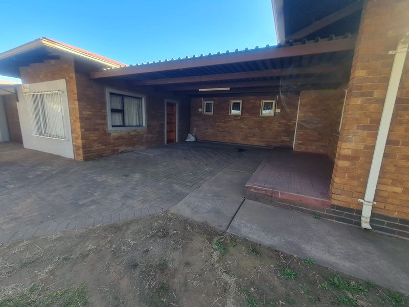 Front exterior view of the house featuring a brick facade, paved driveway, and a covered carport area with a small tiled porch.
