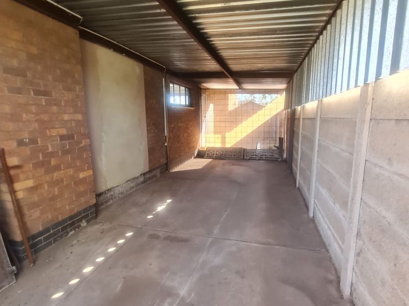 A functional, open-sided garage structure featuring a corrugated metal roof, exposed steel beams, and a combination of face brick and precast concrete walls.